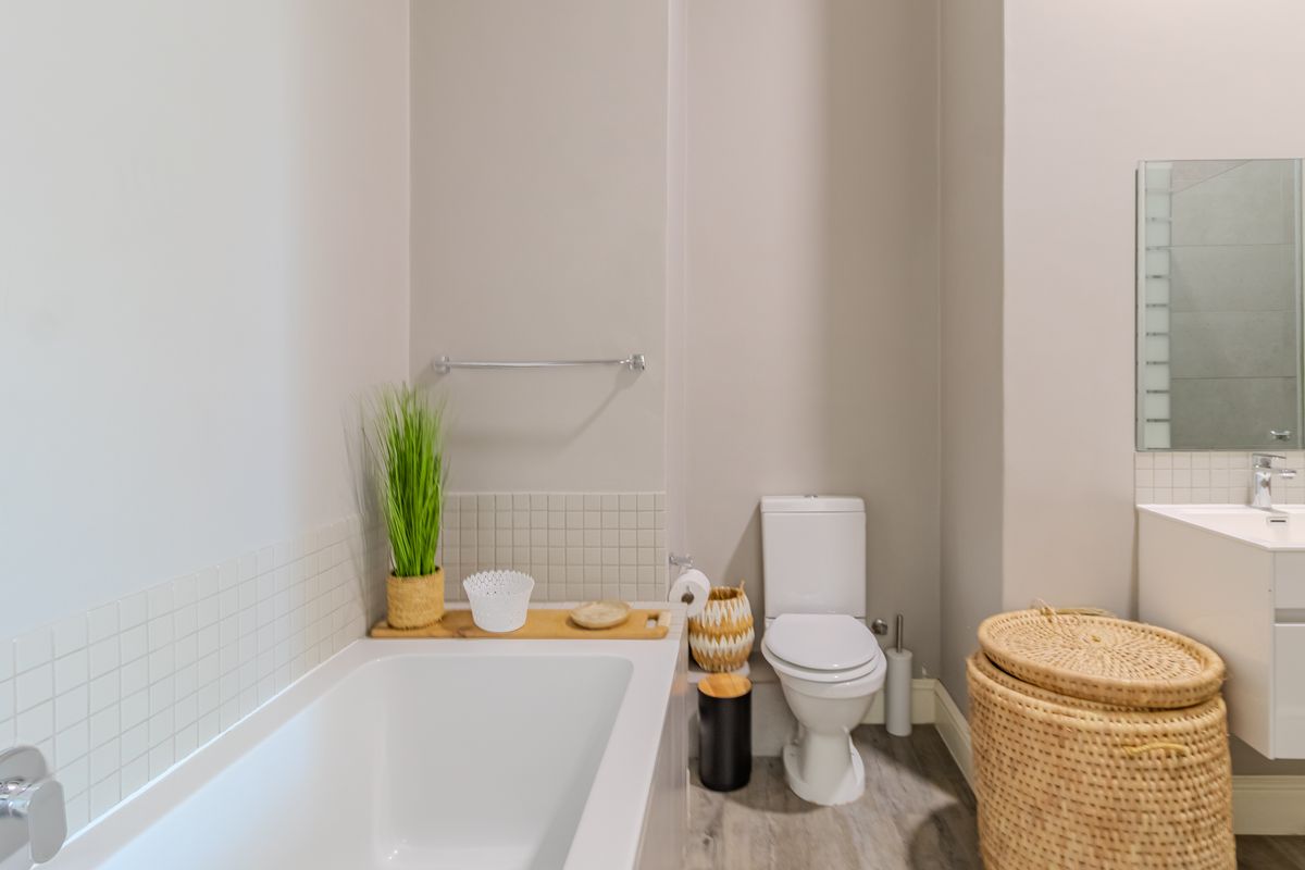 A clean and modern bathroom featuring a built-in bathtub, a wall-mounted vanity with a basin, and a standard toilet.