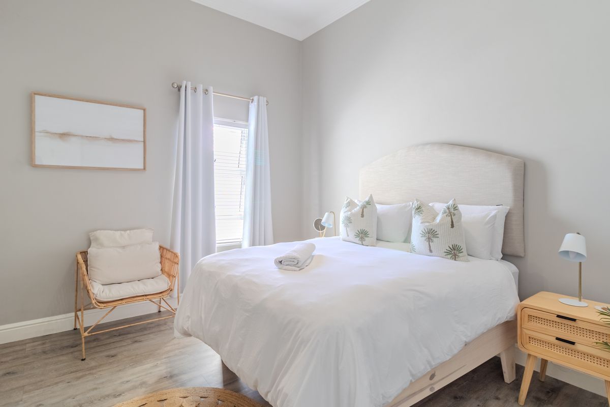 A bright and well-maintained bedroom featuring neutral wall tones, wood-look flooring, and a window with fitted curtains.