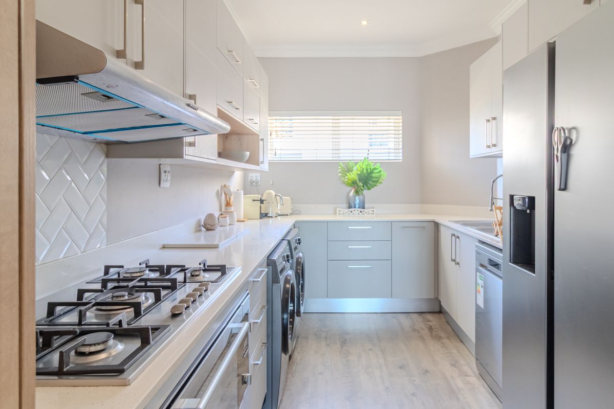Modern kitchen featuring light-toned cabinetry, stone countertops, a gas hob, built-in oven, extractor fan, and integrated laundry appliances.