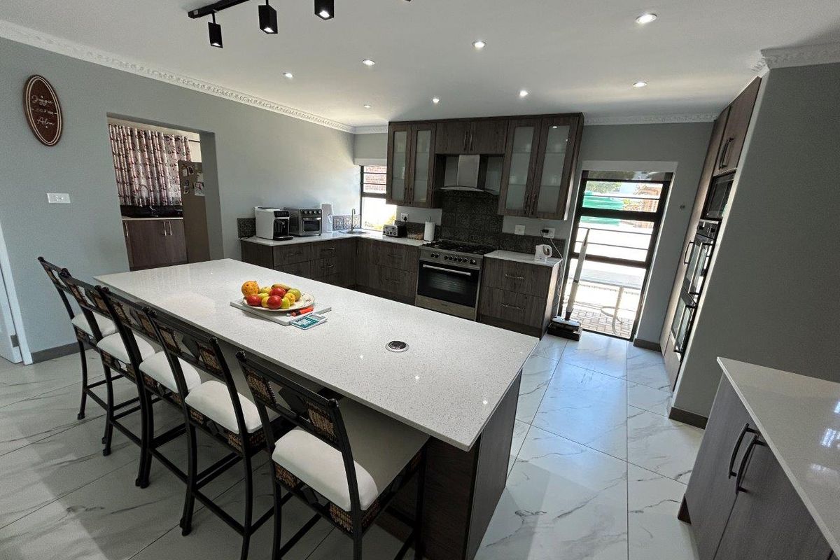 Modern kitchen featuring a large central island with quartz countertops, dark wood cabinetry, built-in appliances, and sleek marble-look floor tiles.