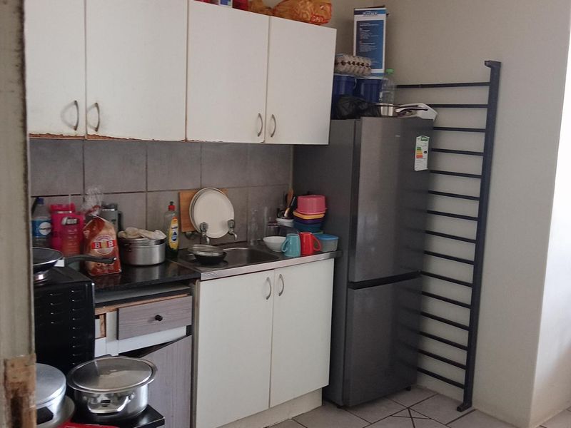 Compact kitchen area featuring white cabinetry, tiled backsplash, stainless steel sink, and tiled flooring.