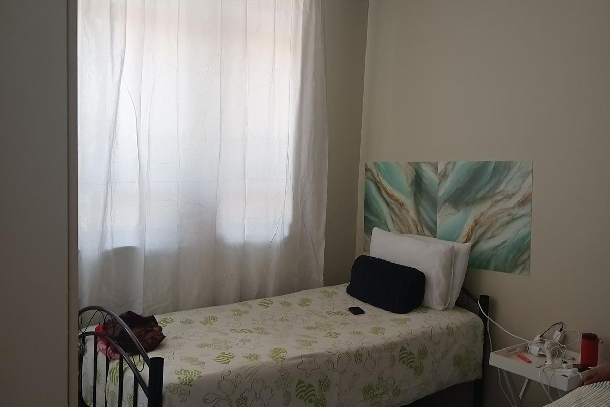 A bedroom featuring tiled flooring and a drop ceiling, providing a functional sleeping space with natural light from the window.