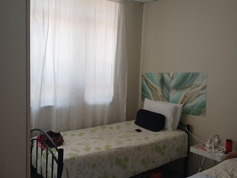 A bedroom featuring tiled flooring and a drop ceiling, providing a functional sleeping space with natural light from the window.