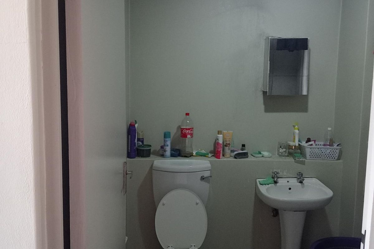 A compact bathroom featuring a pedestal sink, a standard toilet, and tiled flooring, requiring cosmetic updates to improve its overall condition.