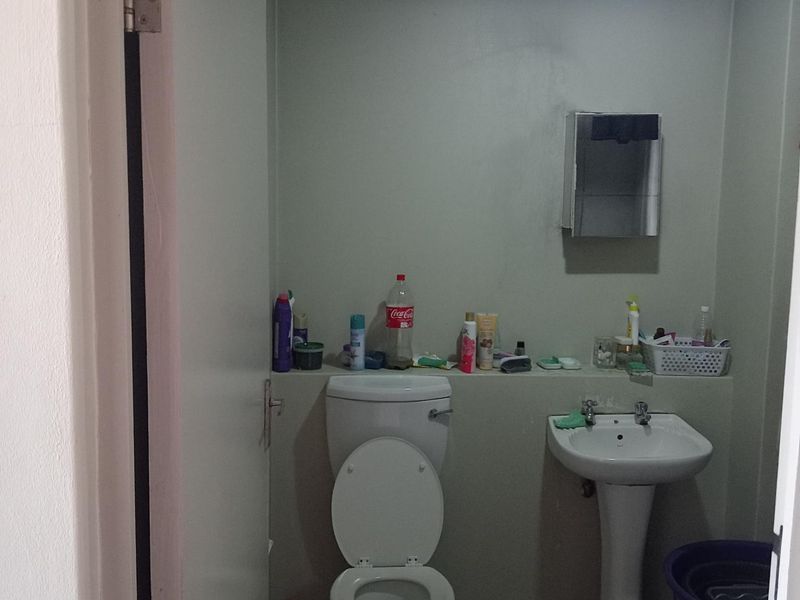 A compact bathroom featuring a pedestal sink, a standard toilet, and tiled flooring, requiring cosmetic updates to improve its overall condition.