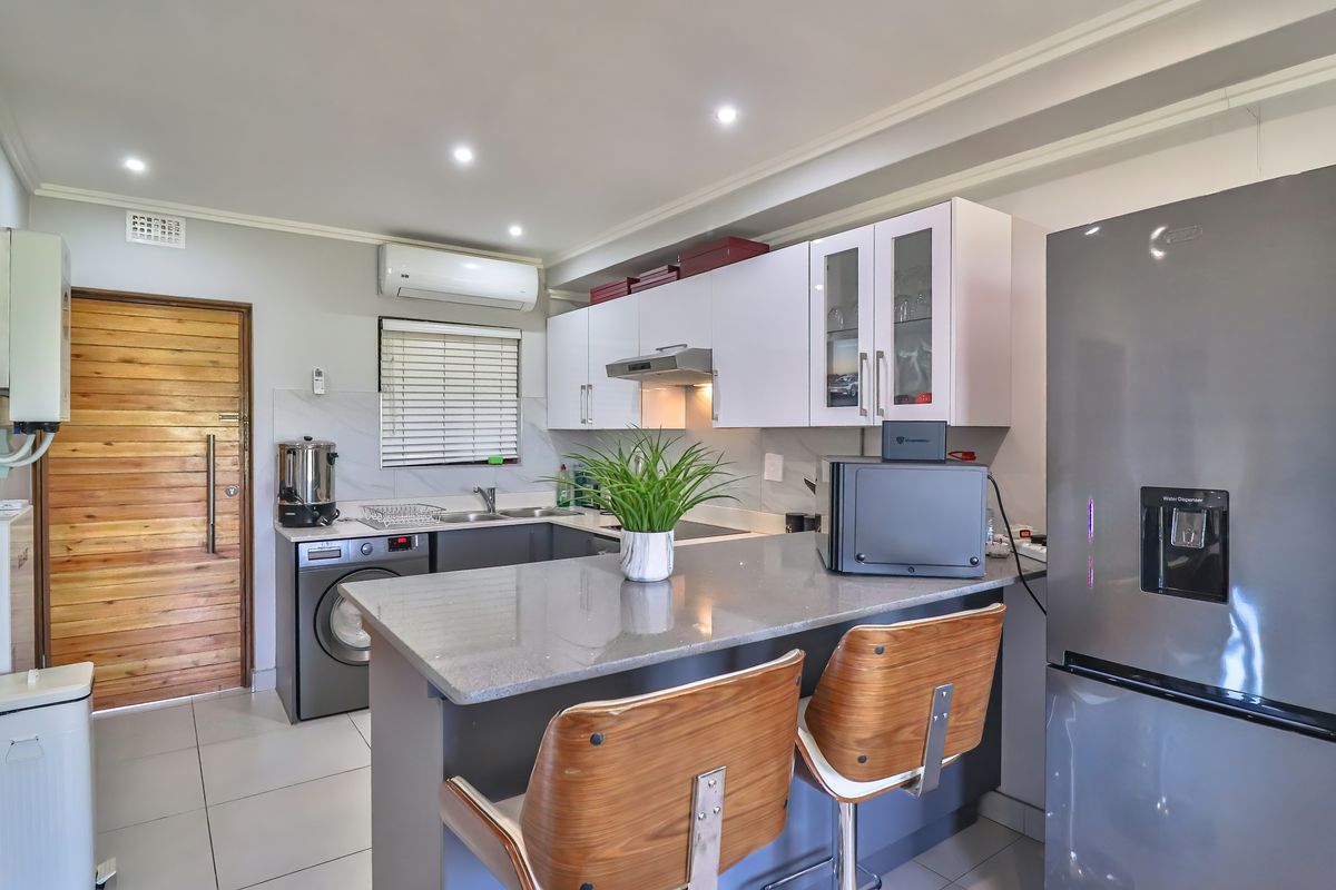 Modern kitchen featuring stone countertops, white cabinetry, integrated appliances, and a breakfast bar, seamlessly integrated into an open-plan living space.