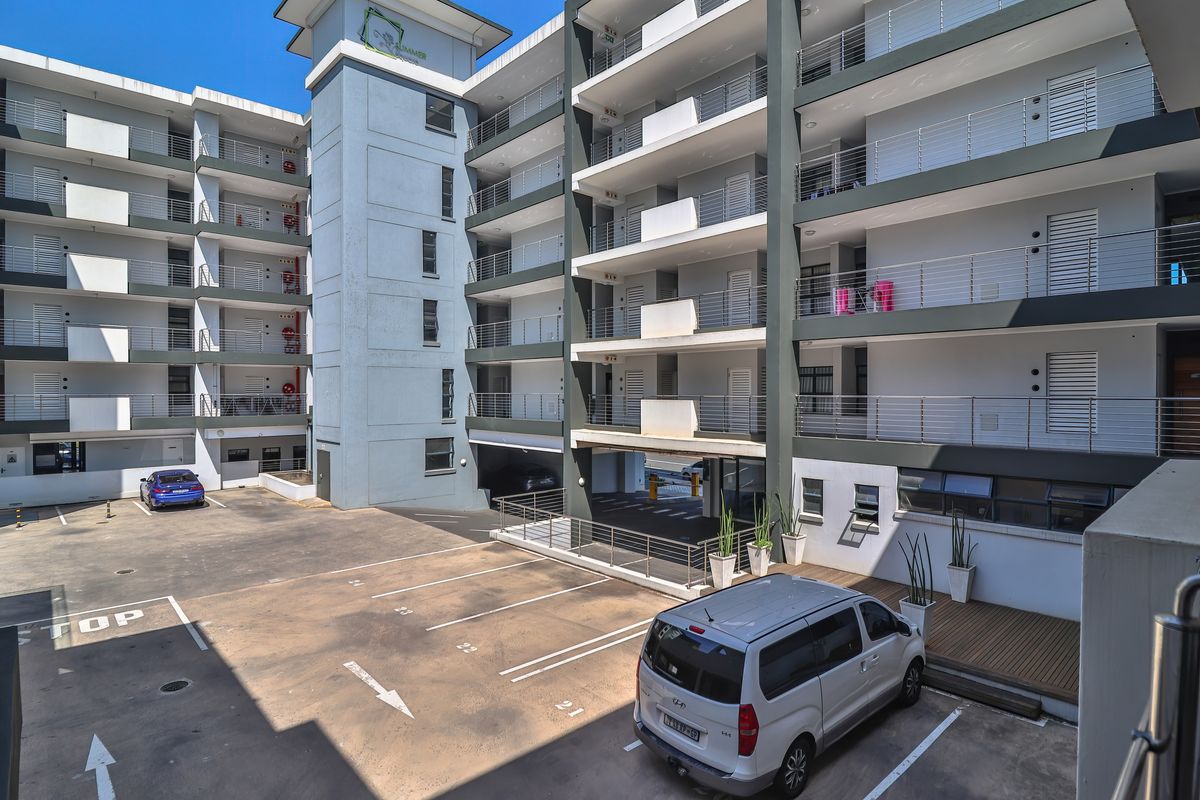 Exterior view of a modern apartment complex featuring multi-level balconies, paved parking area, and structured building facade.