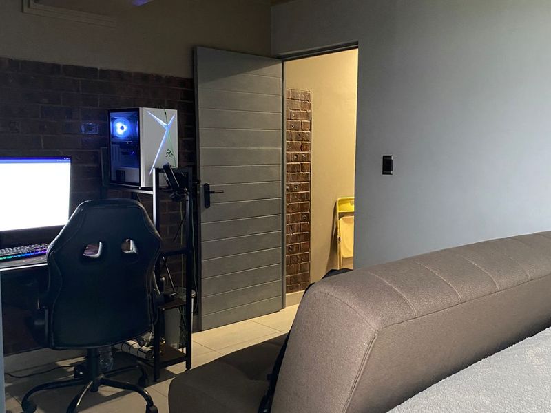 A bedroom featuring exposed brick wall accents, tiled flooring, and a modern grey interior door leading to an adjacent space.