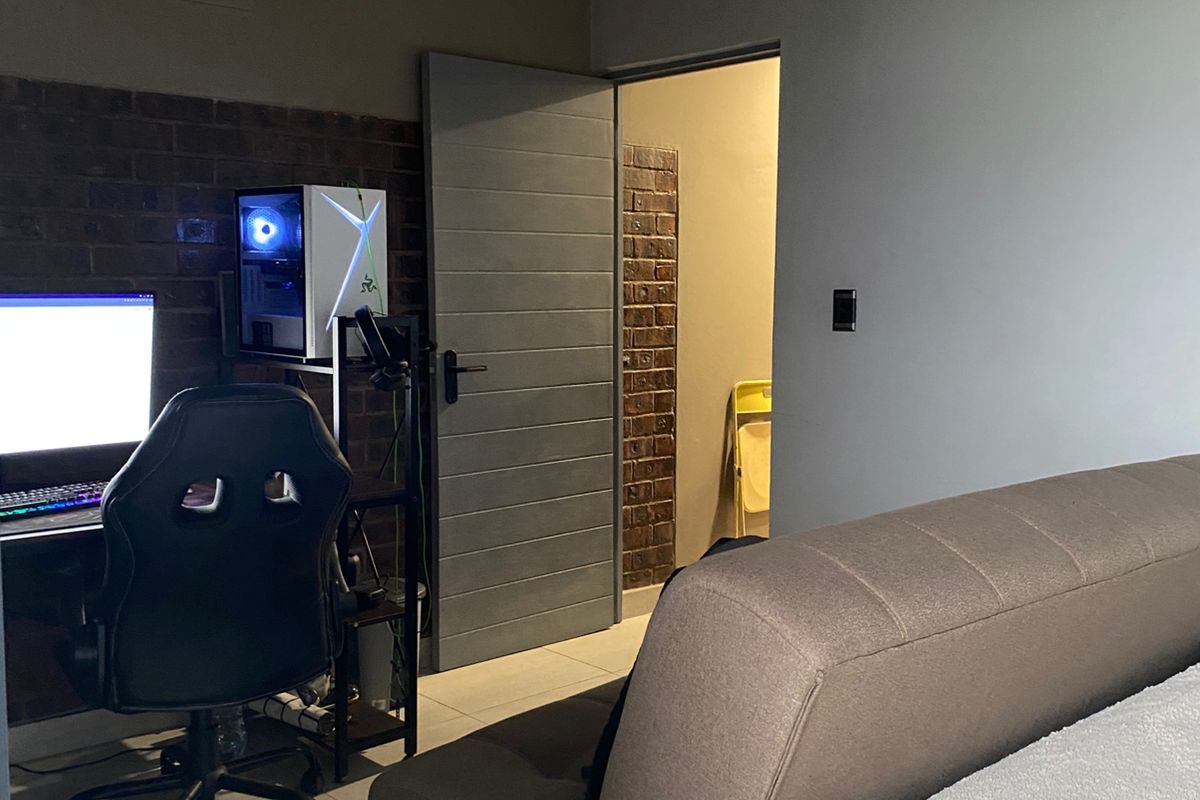 A bedroom featuring exposed brick wall accents, tiled flooring, and a modern grey interior door leading to an adjacent space.
