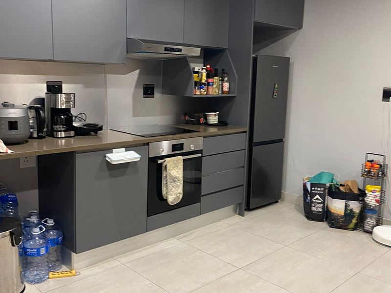 Modern kitchen featuring sleek grey cabinetry, integrated oven, electric hob, extractor fan, and tiled flooring in an open-plan layout.
