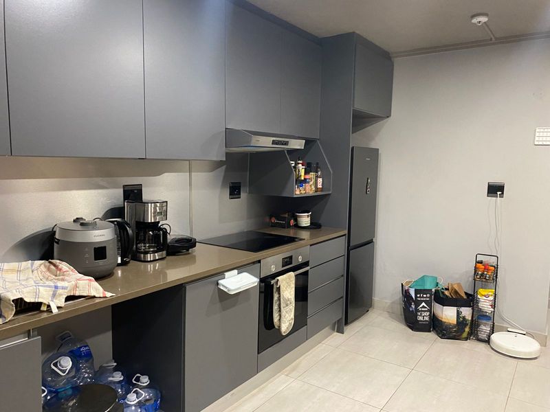 Modern kitchen featuring sleek grey cabinetry, integrated oven, induction cooktop, extractor fan, and stone-look countertops with tiled flooring.