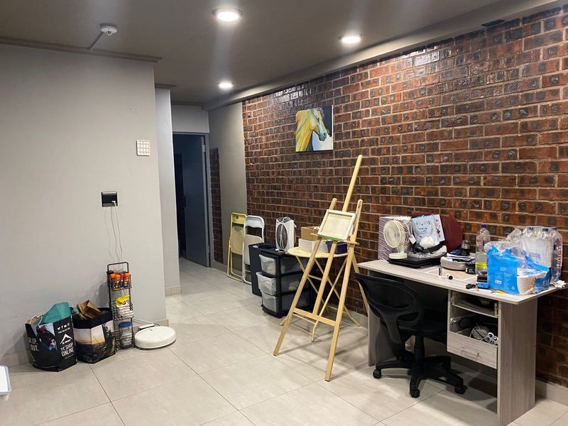 A living area featuring a prominent exposed brick feature wall, recessed ceiling lighting, and neutral floor tiling.