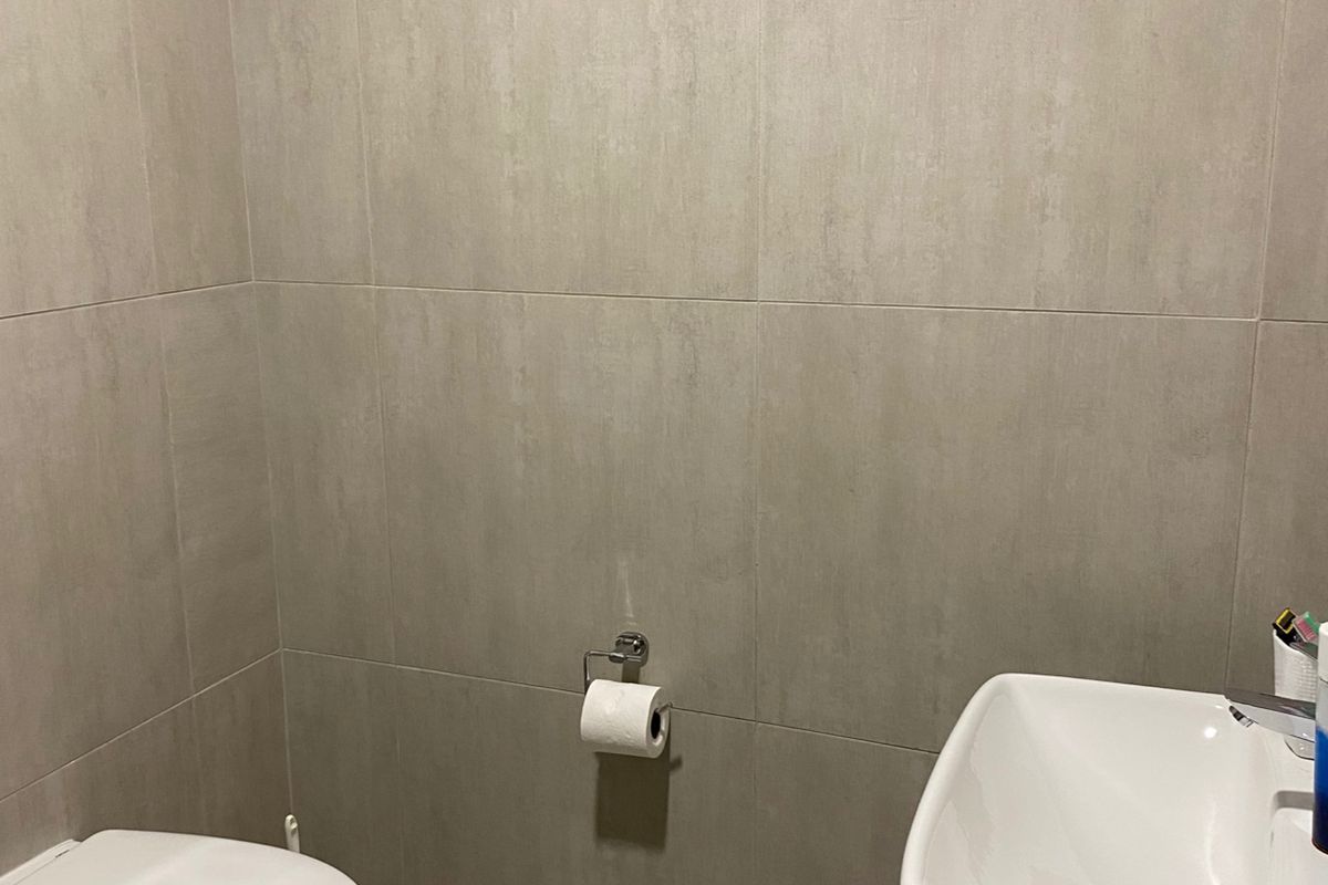 A modern guest bathroom featuring neutral wall tiles, a wall-mounted toilet, and a sleek vanity basin.
