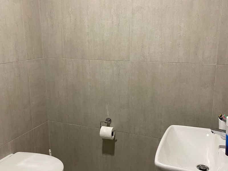A modern guest bathroom featuring neutral wall tiles, a wall-mounted toilet, and a sleek vanity basin.