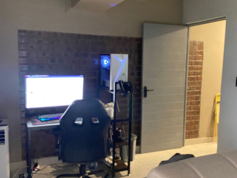 A functional office space featuring an exposed brick feature wall, tiled flooring, and a modern internal door leading to an adjacent room.