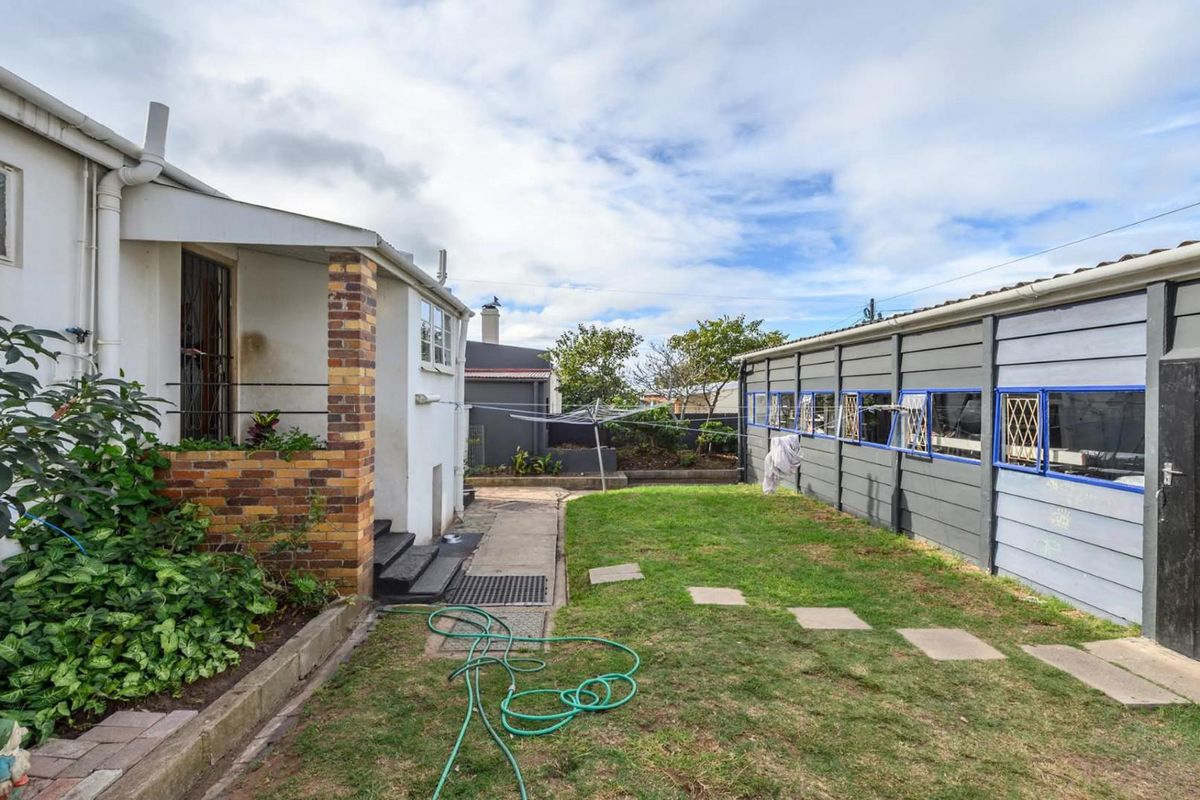 A rear garden area featuring a lawn, paved pathway, and a long boundary wall with integrated windows, adjacent to the main house structure.