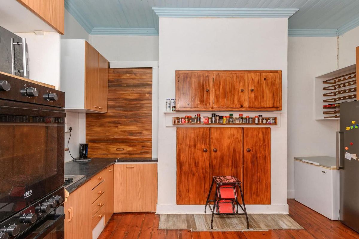 A functional kitchen featuring timber cabinetry, built-in oven, dark countertops, and original timber flooring with a distinctive blue-painted ceiling.