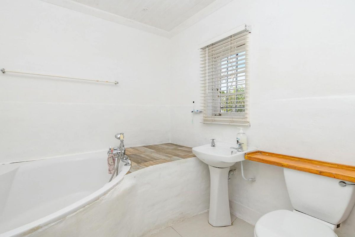 A functional bathroom featuring a pedestal basin, toilet, and a built-in bathtub with a tiled surround and window blinds.