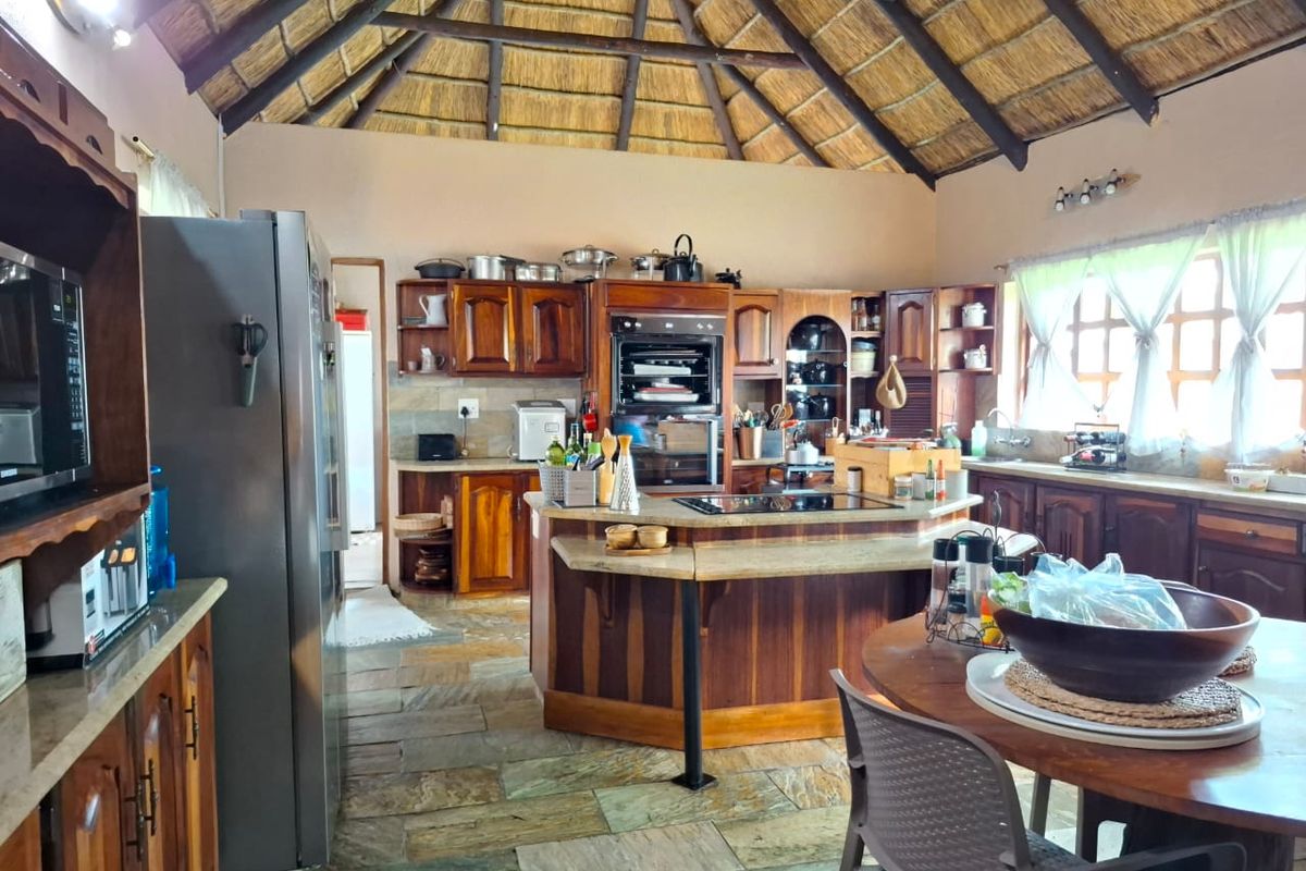 Spacious kitchen featuring a high thatched roof, wooden cabinetry, a central island with a built-in hob, and stone tile flooring.