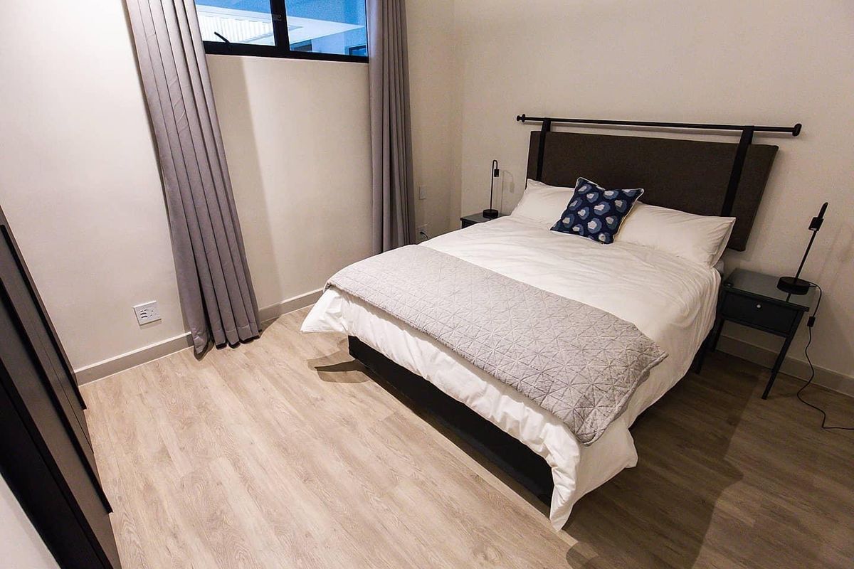 A well-maintained bedroom featuring light wood-look flooring, neutral walls, and a large window with floor-to-ceiling curtains.