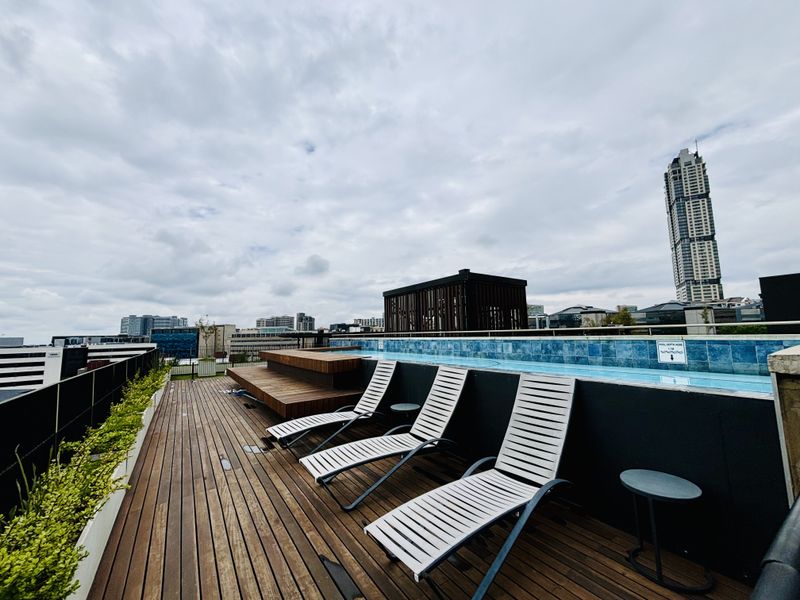 Rooftop swimming pool area featuring a timber deck, modern tiled pool edge, and panoramic city skyline views.