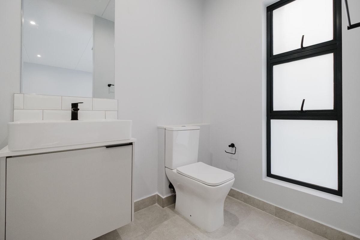 Modern bathroom featuring a sleek vanity with a vessel sink, contemporary toilet, and a large window with black framing.