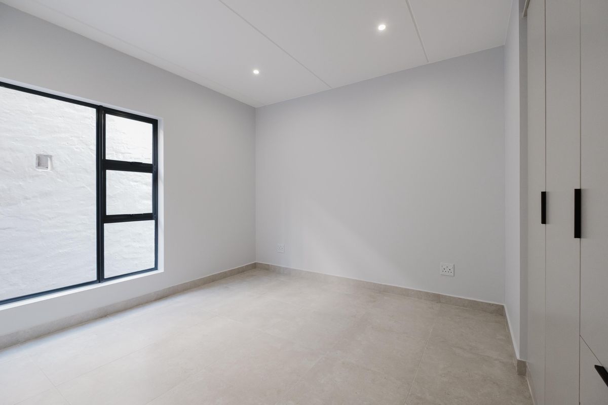 A bright, modern, and empty bedroom featuring neutral tiled flooring, recessed ceiling lighting, and built-in cabinetry with a sleek black handle finish.