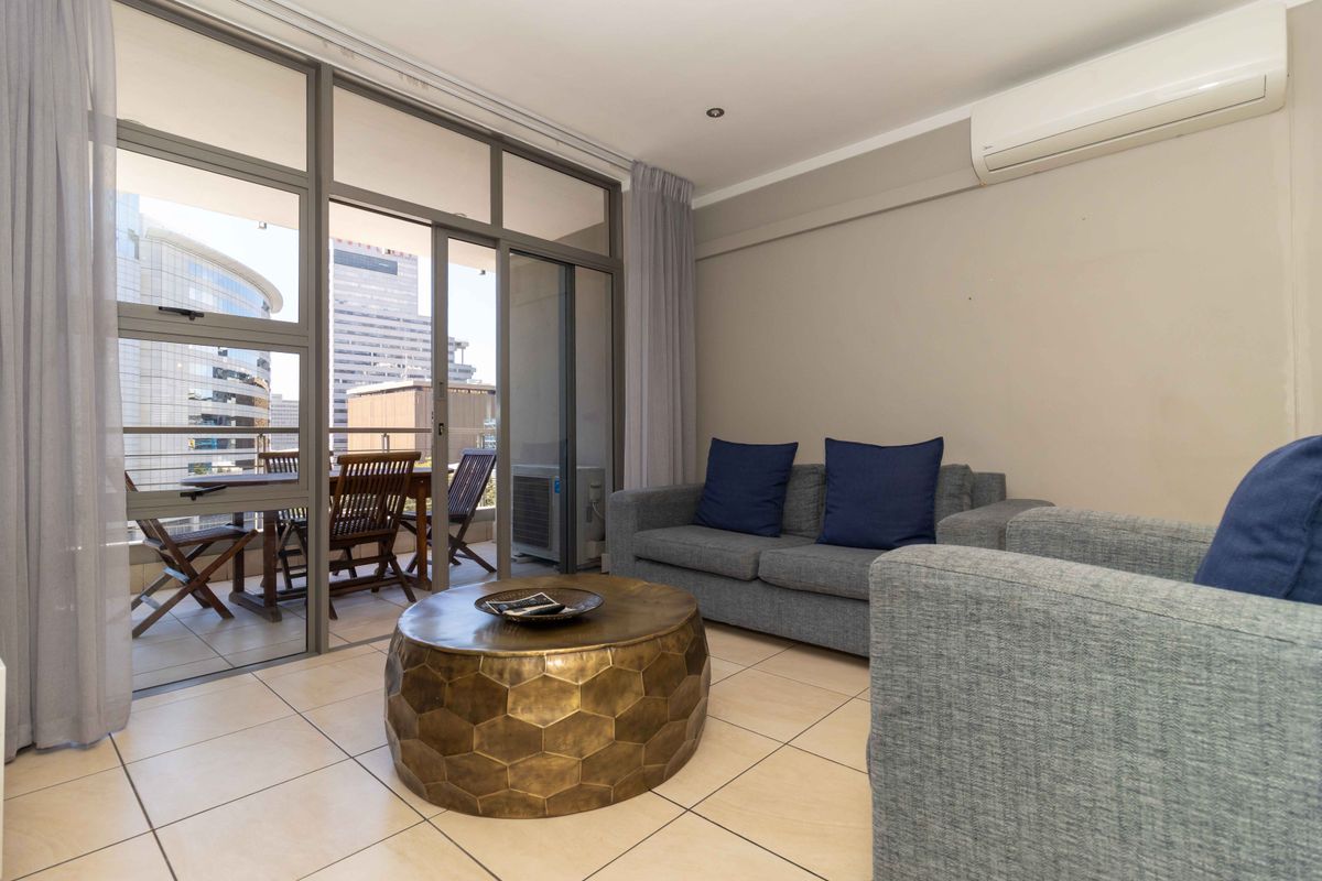 A bright living room featuring large glass sliding doors that open onto a private balcony, complemented by a wall-mounted air conditioning unit.