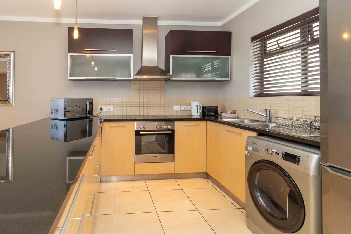 A functional kitchen featuring light wood cabinetry, dark granite countertops, a built-in oven, stainless steel extractor fan, and tiled flooring.