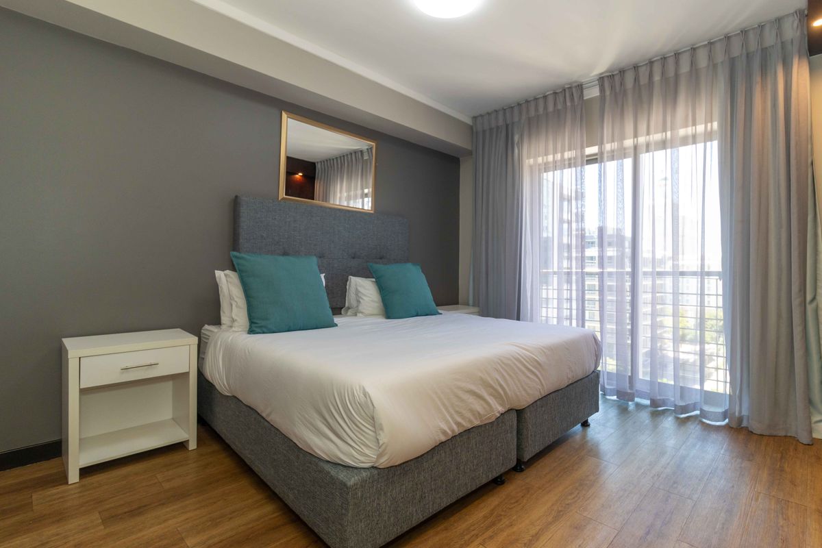 A well-maintained bedroom featuring wood-look flooring, a neutral grey accent wall, and large sliding glass doors providing access to a private balcony.