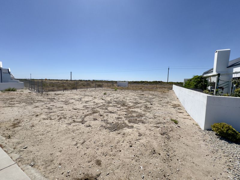A vacant residential plot featuring a perimeter fence and a white boundary wall, offering a clear space for potential development.