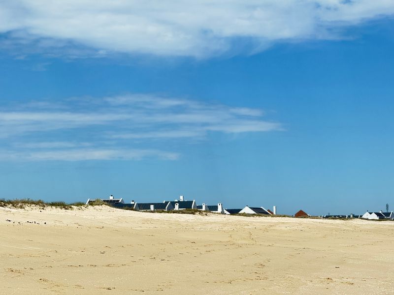 A scenic view of the coastal landscape featuring sandy dunes in the foreground and residential properties in the distance.