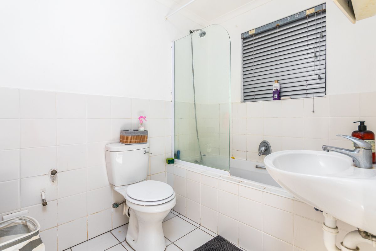 A functional bathroom featuring a combined shower and bathtub, a standard toilet, and a pedestal sink with tiled walls and flooring.