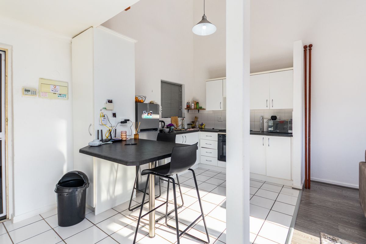 Compact kitchen featuring white cabinetry, dark countertops, built-in oven, and tiled flooring, integrated into an open-plan living space.