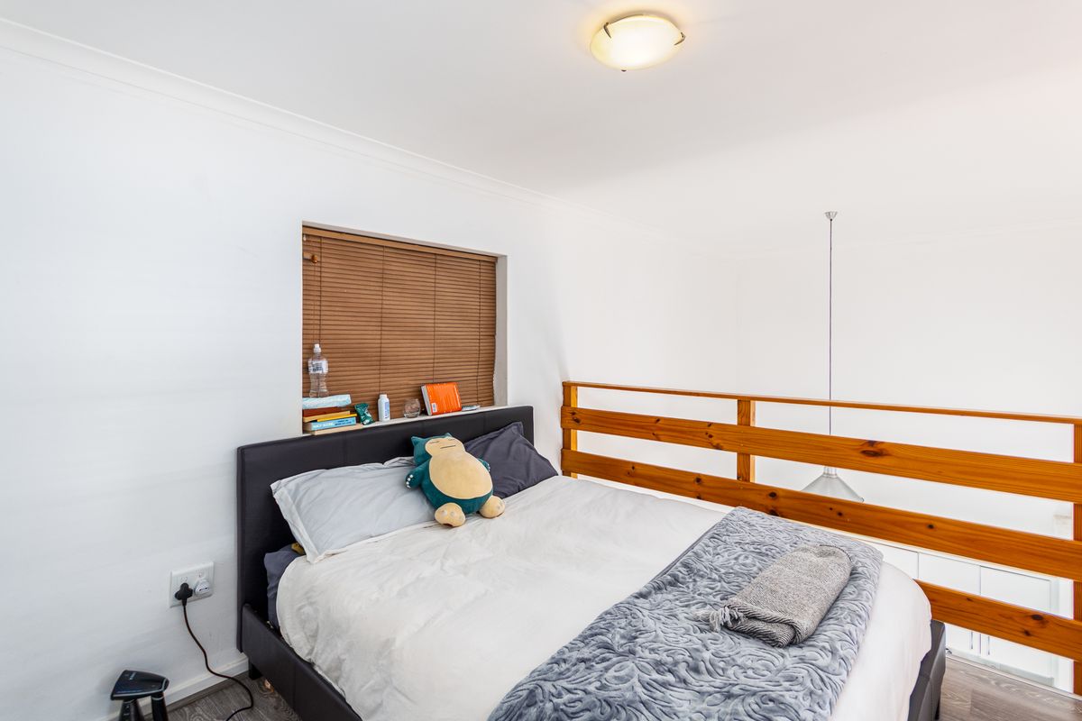 A loft-style bedroom featuring a wooden balustrade overlooking the lower level, fitted with a ceiling light and a recessed window with blinds.