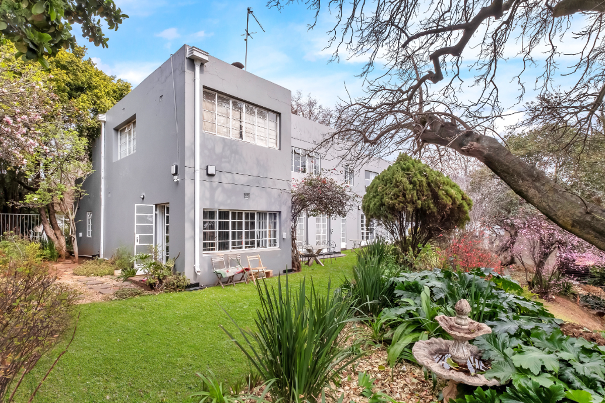Rear view of a two-story residential property featuring a well-maintained garden, mature trees, and classic steel-framed windows.