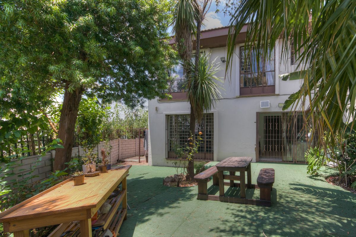 Rear exterior view of the townhouse featuring a private garden area with artificial turf, security gates, and sliding door access to the main living space.