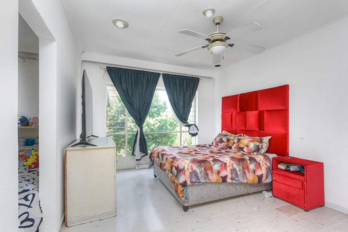 A bedroom featuring a ceiling fan, recessed lighting, and large windows with security bars, offering a functional space with potential for cosmetic updates.