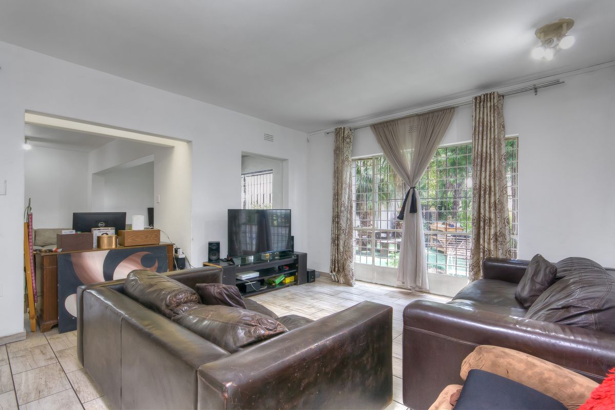 Spacious living room featuring tiled flooring and large windows with security gates, offering natural light and a view of the garden area.