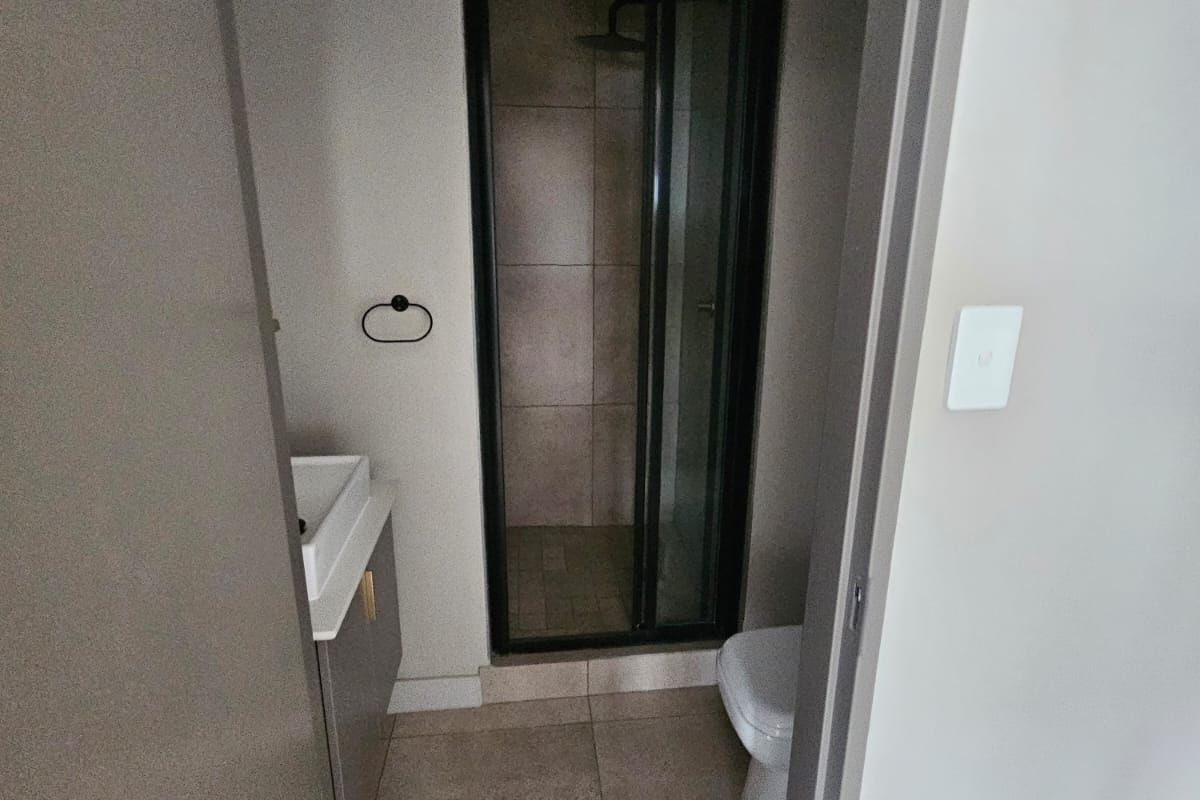 A modern, compact bathroom featuring a walk-in shower with a black frame, a vanity basin, and a toilet, finished with neutral floor tiles.
