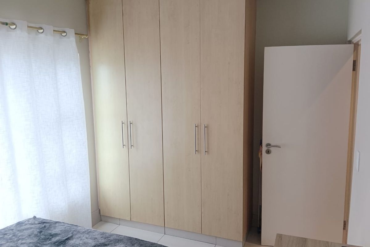 A bedroom featuring built-in light wood-finish wardrobes, tiled flooring, and a standard interior door.