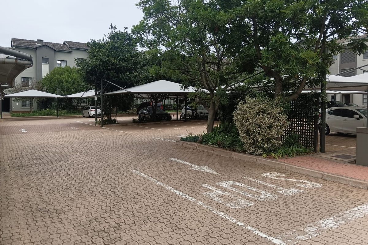 A paved parking area featuring covered carports and established landscaping within the apartment complex grounds.
