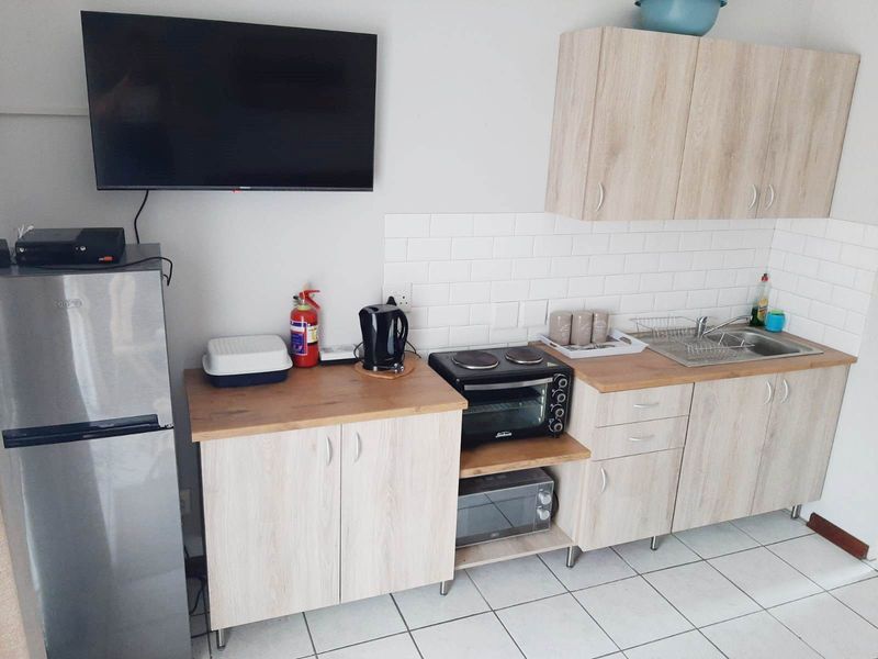 Compact kitchenette featuring light-wood cabinetry, subway tile backsplash, laminate countertops, and a stainless steel sink, providing functional preparation space.