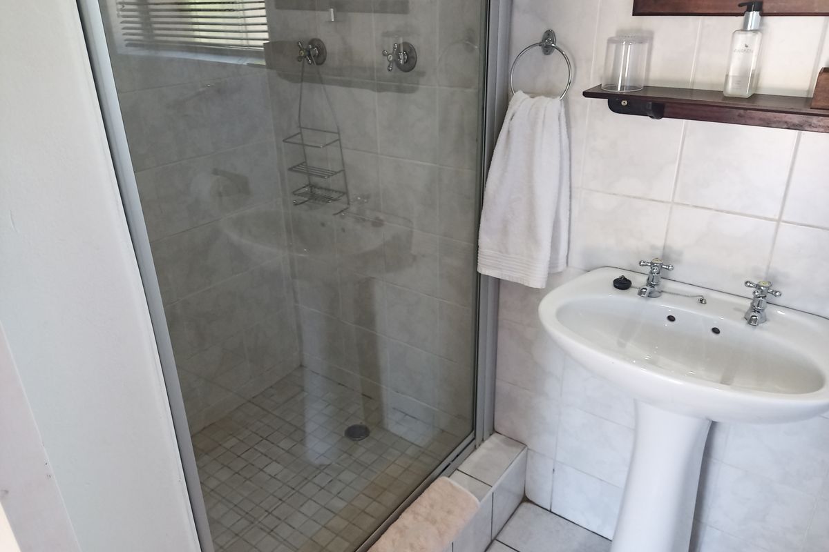 A functional bathroom featuring a pedestal basin, tiled walls, and a glass-enclosed shower unit with standard fixtures.