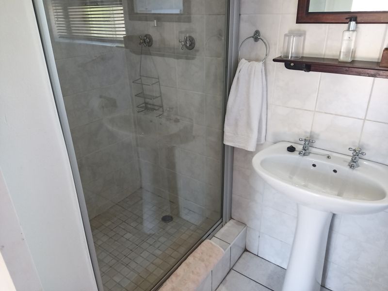 A functional bathroom featuring a pedestal basin, tiled walls, and a glass-enclosed shower unit with standard fixtures.