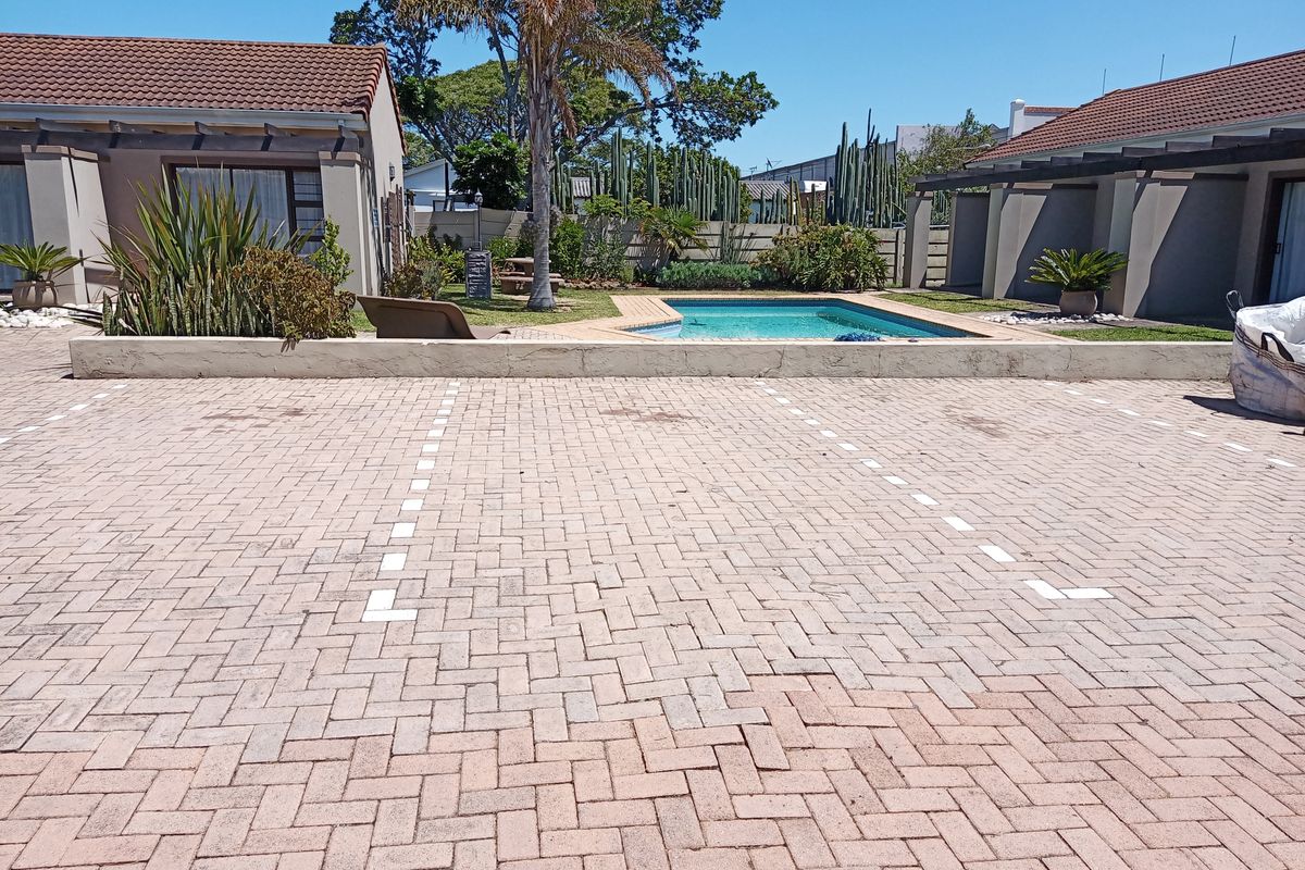 Rear exterior view featuring a paved parking area, a swimming pool, and a pergola structure set within a landscaped garden.