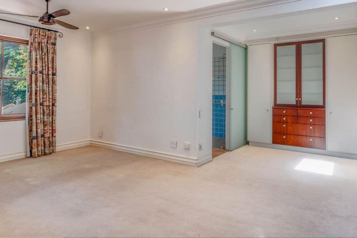 Spacious bedroom featuring neutral carpeting, built-in cabinetry, a ceiling fan, and direct access to an en-suite bathroom with a sliding glass door.
