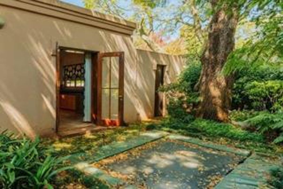 A view of the rear exterior facade featuring a paved patio area, mature trees, and direct access through wooden French doors.