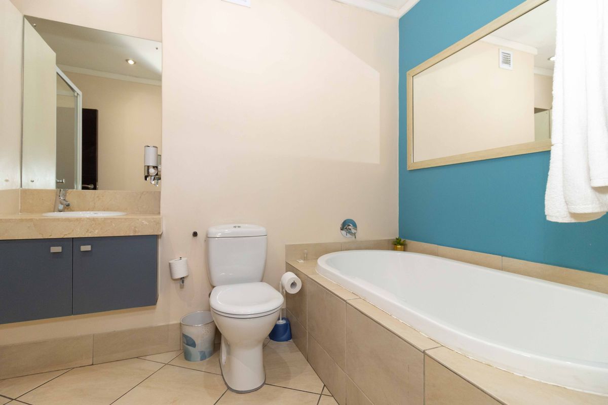 A functional bathroom featuring a built-in bathtub, vanity with stone countertop, toilet, and wall-mounted mirror with blue accent wall.