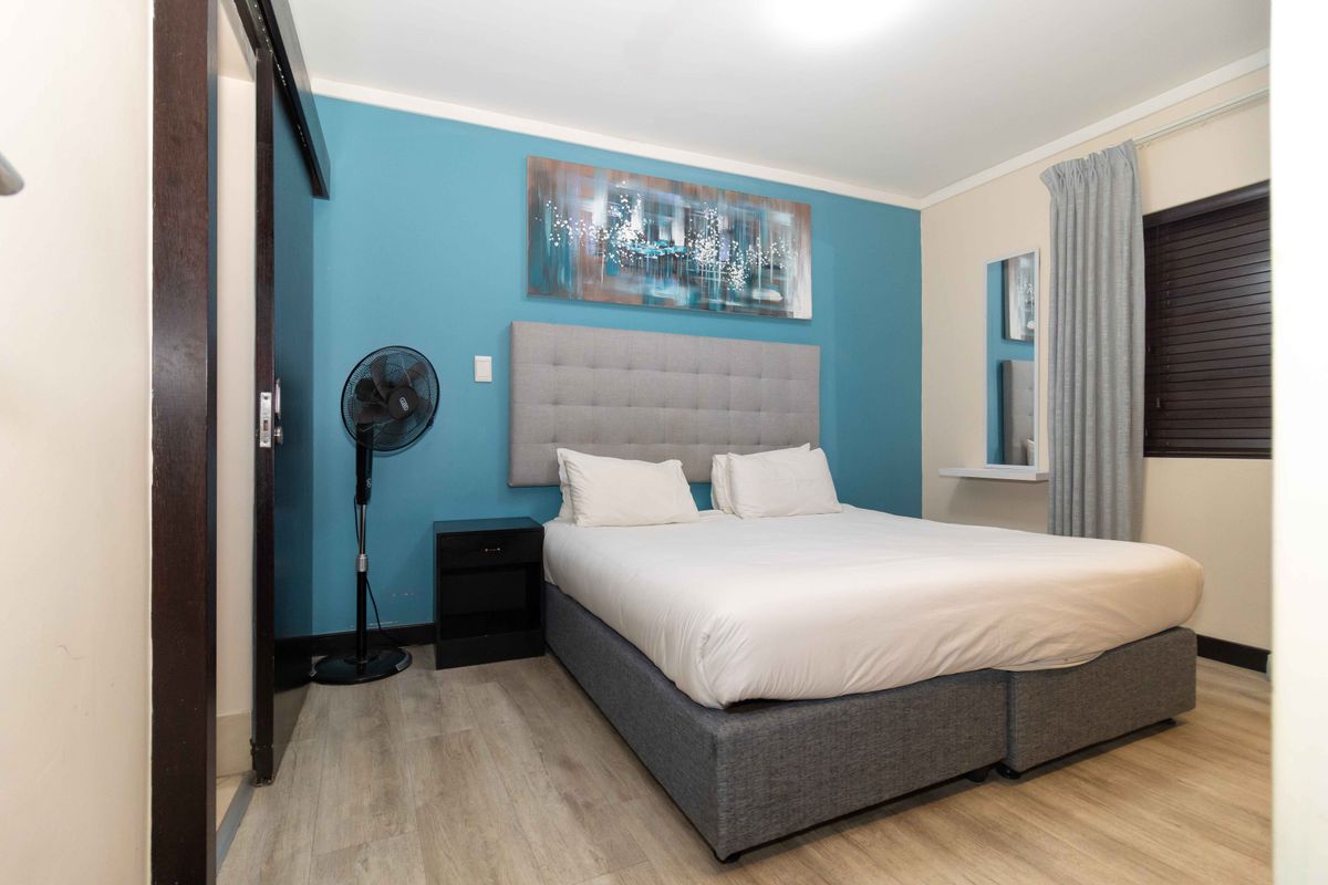 A well-maintained bedroom featuring light wood-look flooring, a blue accent wall, and a sliding door entrance.